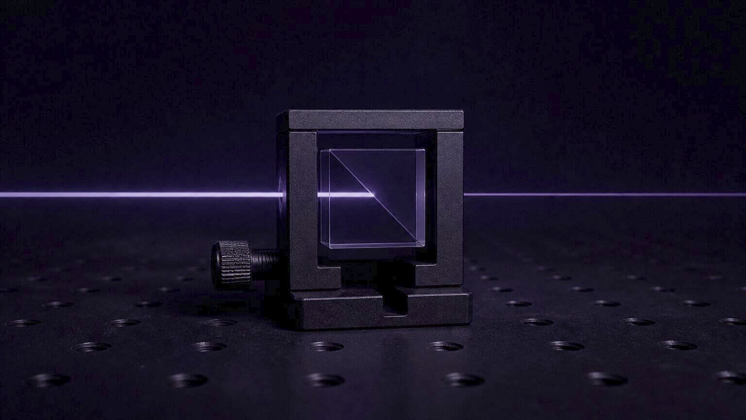 A glass beam-splitter cube in a matte black mount on a dark optical breadboard. One violet beam enters from the left, brightens on the diagonal inside the cube, and one beam leaves to the right.