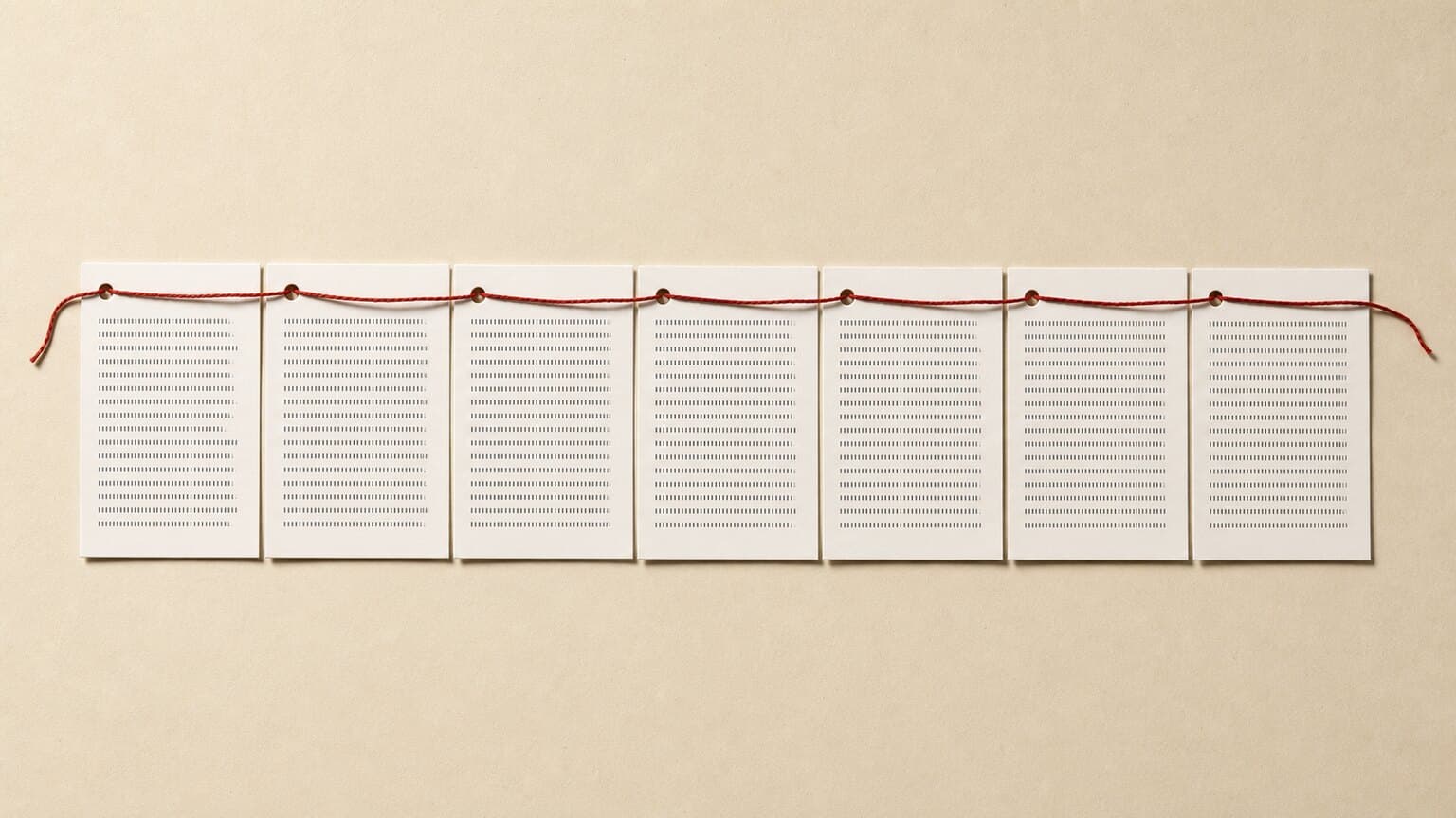 Seven identical printed sheets laid in a row across a desk, each punched with one hole, all strung on a single unbroken red thread.